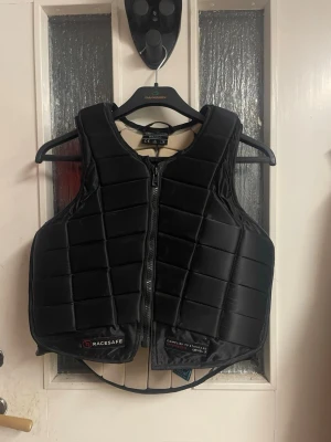 Svart skyddsväst från Racesafe - Säljer en svart skyddsväst från Racesafe. Använd ett flertal gånger och lite smutsig på insidan (se bild). Förövrigt fint skick. Strl vuxen x-s. Nypris ca 3549kr