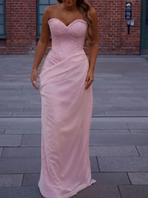 Ljusrosa långklänning med pärlor - Elegant ljusrosa långklänning med hjärtformad urringning och pärlbroderier på överdelen. Klänningen är axelbandslös och har ett omlottliknande lager av tunt tyg över kjolen för en extra lyxig känsla. Perfekt för speciella tillfällen. Den är special sydd i Kosovo i storlek 34/36, endast använd en gång & kemtvättad🩷