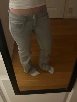 Lowaist Ljusgrå bootcut jeans - Säljer ett par ljusgrå jeans med bootcut passform och med dubbelknapp. I storlek 152 men passar jättebra på mig med storlek 32