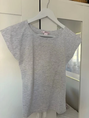 Ljusgrå topp med öppen rygg och knyt - Snygg ljusgrå topp med korta ärmar och rund halsringning. Baksidan har en öppen design med knyt längst ner, perfekt till sommaren🌊💕 