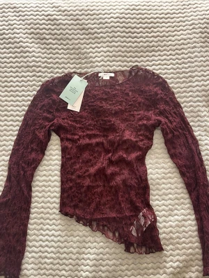 Vinröd spetsblus - Snygg vinröd långärmad spetsblus från Gina Tricot med transparent material och asymmetrisk nederkant. Perfekt för dig som vill ha en unik och trendig topp med coola detaljer. Blusen har rund halsringning och är figurnära i modellen.