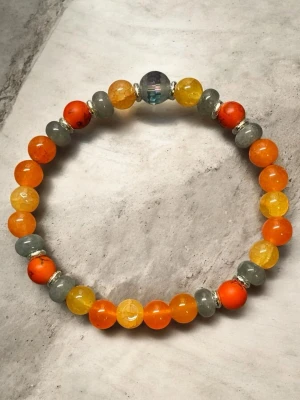 Färgglatt pärlarmband i orange och grått - Snyggt armband med runda pärlor i orange, gult och grått. Armbandet har en större, skimrande pärla i mitten och små silverfärgade detaljer mellan pärlorna. Perfekt accessoar för att addera färg till din stil.