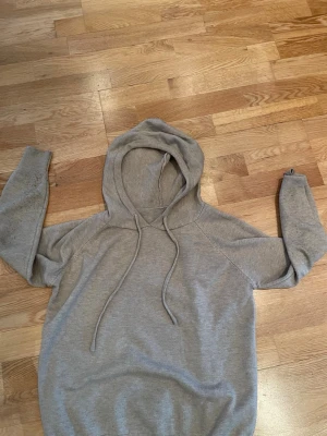 Grå och beige kashmire hoodies - En enkel och stilren grå hoodie med huva och dragsko. Hoodien har långa ärmar och ribbade muddar vid ärmslut och nederkant. Perfekt för en avslappnad look och passar till det mesta. Materialet känns mjukt och bekvämt.