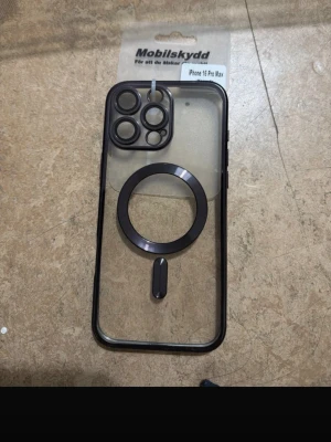 Transparent magsafe skal iPhone 16 Pro Max - Snyggt transparent mobilskal från Mobilskydd till iPhone 16 Pro Max med svart ram och MagSafe-ring. Skalets baksida är genomskinlig och har förstärkt skydd för kameralinserna. Perfekt för dig som vill visa upp mobilen men ändå ha bra skydd och MagSafe-kompatibilitet.