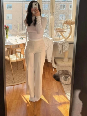 Vida vita byxor med hög midja - Säljer ett par stilrena, vida byxor i vitt med hög midja och pressveck framtill. Byxorna har raka ben och diskreta fickor i sidorna. Perfekta för en clean och trendig look. Materialet ser ut att vara mjukt och följsamt, troligen polyesterblandning.
