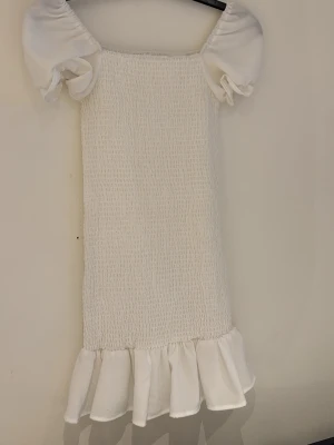 Vit kort klänning - Supersöt vit kort klänning med puffärmar och volangkant nedtill. Klänningen är stretchig så den formar sig efter kroppen. 