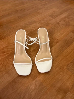 Vita strappy pumps från Boohoo - Snygga vita pumps från Boohoo med tunna remmar och fyrkantig tå. Skorna har en elegant klack och öppen design som ger en trendig look.