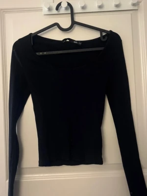 Svart ribbad långärmad topp - En svart, ribbad långärmad topp med rundad halsringning. Toppen har en tight passform och är perfekt att styla med både jeans och kjol. Enkel och stilren design som passar till många olika looks.