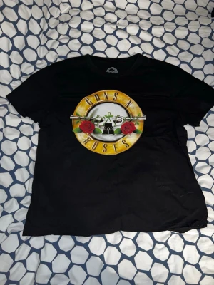 Guns N' Roses svart t-shirt - Svart t-shirt med stort Guns N' Roses-tryck framtill och turnédatum på ryggen. Rund halsringning och klassisk passform. Perfekt för dig som älskar bandmerch och vill sticka ut med en ikonisk look.
