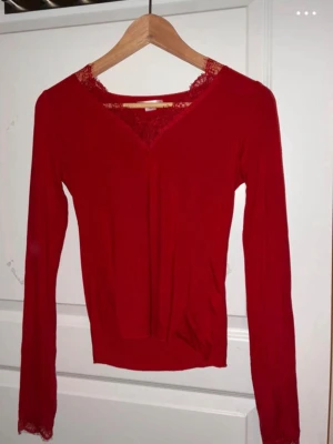 Röd långärmad topp med spets - Snygg röd långärmad topp med v-ringning och spetsdetaljer vid halsringning och ärmslut. Perfekt för dig som vill ha en enkel men ändå elegant look. Tunn och mjuk i materialet, sitter snyggt på kroppen.