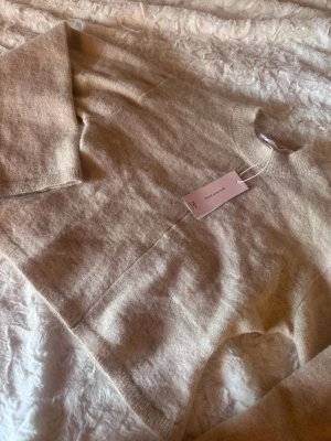 Beige stickad tröja från Arket - Mysig beige stickad tröja från Gina Young 14+ teen i mjuk ullblandning. Tröjan har rund halsringning, långa ärmar och ribbade muddar vid ärmslut och nederkant. Köpt för 300kr och aldrig använd. Säljer pga att den inte passar. 