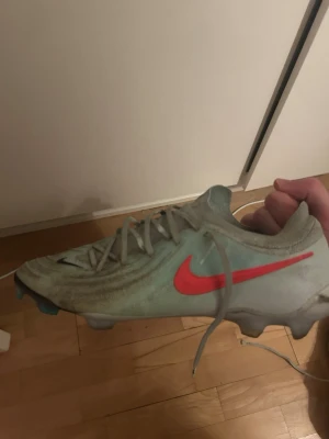 Nike Phantom fotbollsskor grå/röd - Säljer ett par Nike phantom fotbollsskor i ljusgrått med en tydlig röd Nike-swoosh på sidan. Skorna har snörning och dobbar för spel på gräs. Snygg, slimmad design som ger bra grepp och kontroll på planen. Perfekta för dig som vill ha stilrena och funktionella skor. Köpta för 3000 sek, spelat med de i 5 månader.