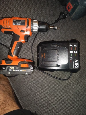 AEG 18V skruvdragare med laddare - AEG skruvdragare i orange och svart med 18V Pro Lithium Ion-batteri och tillhörande laddare. Ergonomiskt handtag och robust design, perfekt för byggprojekt och hemmafix. Laddaren är svart med tydliga indikatorlampor och passar batteriet smidigt.