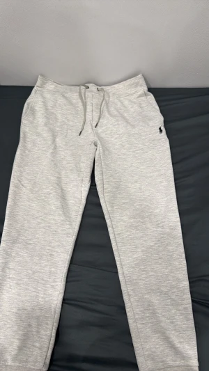 Grå mjukisbyxor från Polo Ralph Lauren - Snygga ljusgrå mjukisbyxor från Polo Ralph Lauren med dragsko i midjan och sidofickor. Klassisk logga broderad på vänster sida. Tillverkade i mjukt och bekvämt material, perfekta för chill dagar. Raka ben och enkel design som passar till det mesta.