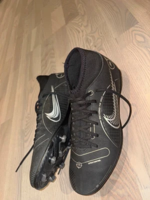 Svarta Nike fotbollsskor med dobbar - Nike Mercurial-fotbollsskor i storlek 40,5, framtagna för hög fart och exakt bollkontroll. De har en lätt sula och ovandel med bra grepp som underlättar snabba vändningar och explosiv acceleration.                      Skorna är sparsamt använda och köptes på rea för 699 kr, perfekt för en smidig och snabb affär.