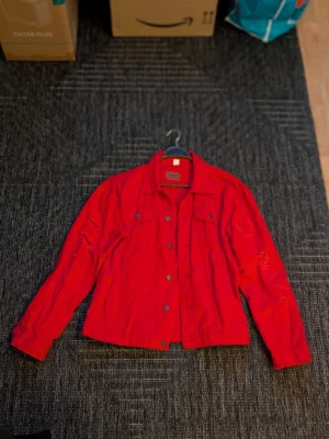 Röd jeansjacka med slitningar M/L - Säljer en röd jeansjacka i mycket fint skick. Använd max 1 gång, i princip som ny. Snygg distressed/sliten design som ger en cool streetwear-look. 🔸 Märkt 4XL, men passar snarare M/L 🔸 Färg: röd 🔸 Knäppning framtill + bröstfickor 🔸 Inget slitage förutom designen 🔸 Rök- och djurfritt hem Pris: 129kr Kan skickas mot frakt eller hämtas upp enligt överenskommelse. Hör av dig vid intresse!