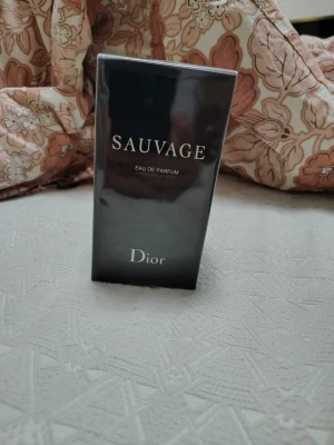 Dior Sauvage Eau de Parfum - Sauvage Eau de Parfum från Dior i en elegant, mörkblå och svart rektangulär kartong med silverfärgade detaljer. Förpackningen har en lyxig känsla och är inslagen i plast. Perfekt för dig som gillar exklusiva dofter.