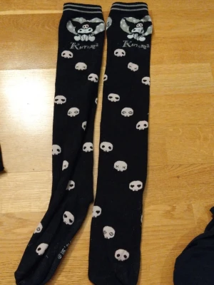 Svarta knästrumpor med dödskallar Kuromi - Långa svarta knästrumpor från Kuromi med vita dödskallemönster och en söt Kuromi-figur upptill. Strumporna har vita detaljer och texten 'Kuromi' vid kanten. Perfekta för dig som gillar edgy och gullig stil. Använda typ 4-5 gånger. Priset kan diskuteras. ❤️ 