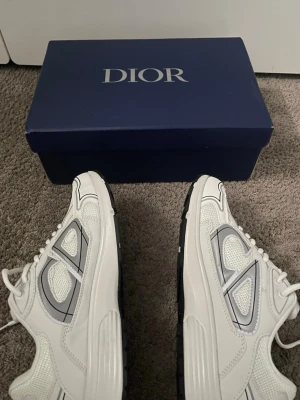 Vita sneakers med grå detaljer - Snygga vita sneakers med grå och svarta detaljer. Skorna har en modern design med cd märken på sidan. Perfekta för dig som vill sticka ut med exklusiva sneakers.