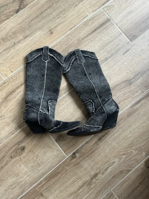 Svarta cowboy boots med mönster - Unika svarta cowboy boots med markerade vita sömmar och prickigt mönster på skaftet. Boots med spetsig tå och bred klack, tillverkade i mocka och skinn. Perfekta för dig som vill sticka ut och addera western-vibe till din stil.