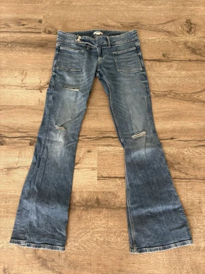 Blå bootcut jeans från Gina Tricot - Säljer ett par blå bootcut jeans från Gina Tricot 14+ med slitna detaljer och stora fickor fram. Jeansen har en klassisk femficksmodell, låg midja. Andvända 2 gånger så i princip helt nya!❤️
