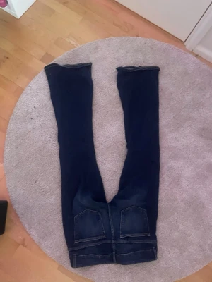 Mörkblå bootcut jeans med slitningar - Säljer ett par mörkblå bootcut jeans med slitningar på knäna och snygga detaljer. Jeansen har fem fickor, låg midja och lätt tvättade partier för en cool look. Perfekta för dig som gillar en avslappnad men trendig stil.