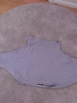 Ljusgrå ribbad polotröja - Ljusgrå polotröja med ribbad struktur och lång ärm. Tröjan har en hög krage och är tillverkad i ett mjukt, stretchigt material som ger en skön passform tajtare vid midjan. Perfekt för lager-på-lager och enkel att matcha med olika outfits.