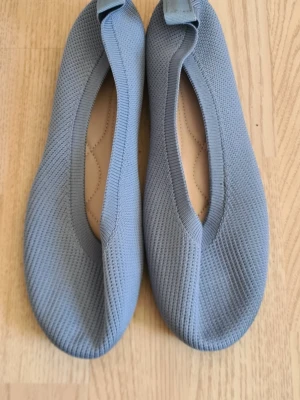 Ljusblå stickade ballerinaskor - Säljer ett par ljusblå ballerinaskor med stickad ovandel och rundad tå. Skorna har en elastisk kant runt öppningen för skön passform och en mjuk innersula. Snygg och enkel design som passar till många outfits.
