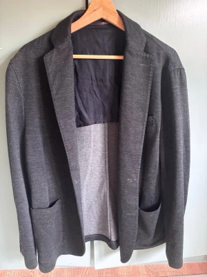 Acne kavaj Maugham AW13 - Stilren mörkgrå kavaj med två stora framfickor och klassisk krage. Kavajen har lång ärm och enkelknäppning framtill. Perfekt för en clean och avslappnad look. Materialet känns mjukt och har en lätt stretch.