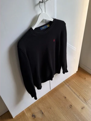 Svart stickad tröja från Polo Ralph Lauren - Klassisk svart stickad tröja från Polo Ralph Lauren med rund halsringning och diskret röd logga broderad på bröstet. Tröjan har ribbade muddar vid ärmslut och nederkant. Perfekt för en stilren och enkel look. Tags samt påse medföljer! Mvh ItsForfits 🌟Skick 9/10