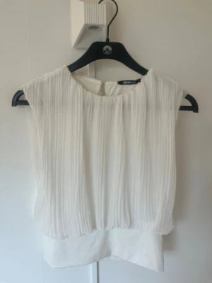 Vit plisserad blus från Gina Tricot - Superfin vit blus från Gina Tricot med plisserad överdel och ärmlös design. Toppen har rund halsringning och en lätt, luftig känsla som passar perfekt till jeans eller kjol. Enkel att styla och ger en fräsch look. Använd 3 gånger. 