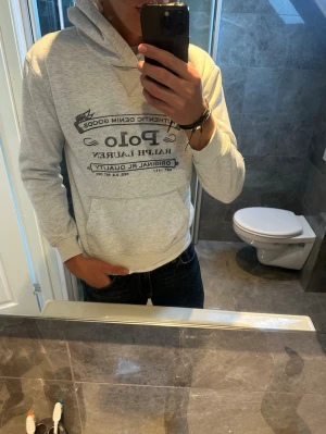 Ljusgrå hoodie från Polo Ralph Lauren - Snygg ljusgrå hoodie från Polo Ralph Lauren med svart tryck framtill. Tröjan är i bra skick utan några skador. Tröjan är i storlek M men sitter mer som en S. Jag på bilden är 188cm och den är något liten på mig. Hör av er vid fler frågor;)