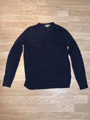 Mörkblå stickad tröja  - En stilren mörkblå stickad tröja  med rund halsringning och långa ärmar. Tröjan har ribbade muddar vid ärmslut och nederkant. I storlek M 