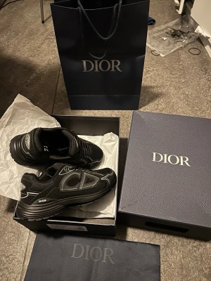 Svarta Dior B30 sneakers helt nya  - Snygga svarta sneakers från Dior med vita och grå detaljer. Skorna har en modern design med mesh och läderpaneler, samt tydlig Dior-logga på sidan och tungan. Perfekta för dig som vill ha en exklusiv och trendig look.