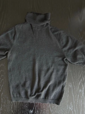 Supergullig svart stickad polotröja - Mysig svart polotröja med  kort ärm. Tröjan är stickad i och har en klassisk, enkel design som funkar till det mesta. Perfekt för dagar när du vill ha något både stilrent och bekvämt.