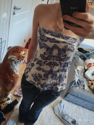 Blåvit mönstrad tubtopp - Säljer en snygg blåvit tubtopp med blommigt mönster. Toppen är axelbandslös och har en bandeauformad passning som sitter tight mot kroppen. Perfekt att styla med jeans eller kjol för en trendig look. ( HEMMA SYDD)