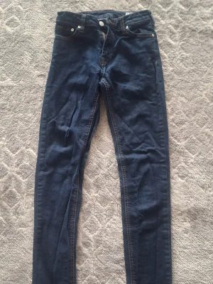 Mörkblå skinny jeans med hög midja - Säljer ett par mörkblå skinny jeans med hög midja och klassisk femficksdesign. Jeansen har smala ben och kontrastsömmar. Perfekta till en avslappnad streetstyle-look. Materialet är stretchigt denim för extra komfort.