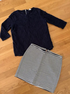 Mörkblå spetsblus med trekvartsärm - Snygg mörkblå blus från i spetsmaterial med trekvartsärm. Blusen har rund halsringning och dragkedja. Kjolen är oanvänd. 30 kr/ styck , 50 för båda.