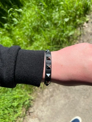 Svart läderarmband med nitar - Coolt svart armband i läder med silverfärgade pyramidnitar runt om. Justerbart spänne för perfekt passform. Perfekt accessoar för en edgy och stilren look.