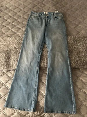 Ljusblå bootcut jeans från ONLY - Säljer ett par ljusblå bootcut jeans från ONLY med klassisk femficksmodell och hög midja. Jeansen har en snygg tvättad look och vida ben som ger en retrovibe. Perfekta till sneakers eller boots för en avslappnad stil.