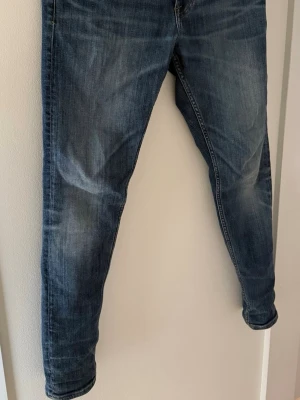 Blå slim fit jeans med tvättade detaljer - Snygga blå slim fit jeans från tiger of sweden med tvättade och slitna detaljer på benen. Klassisk femficksmodell med normalhög midja och smala ben. Jeansen har en cool, något blekt look och passar perfekt till en avslappnad stil.
