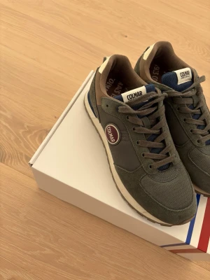 Colmar gröna sneakers herr 42 - Snygga sneakers från Colmar i mörkgrönt med bruna och blå detaljer. Ovandelen är i en mix av mocka och mesh för både stil och komfort. Klassisk Colmar-logga på sidan och vadderad insida för extra skön känsla. Perfekta för dig som gillar streetwear och sportig look. Använda 4 gånger max,jag har kvitto om det önskas