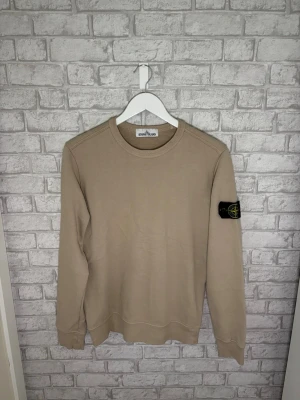 Stone Island tröja - Stone Island crewneck i beige/sand färg. Väldigt fint skick och riktigt clean modell med klassiska badgen på armen. Perfekt casual fit och enkel att matcha.