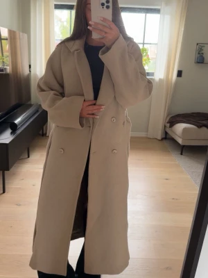 Beige lång kappa med knappar - Stilren beige kappa i lång modell. Väldigt fint skick!🤍 Jag vet inte vilken storlek den är i, men passar mig som har 38!