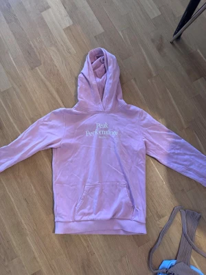 Ljusrosa hoodie från Peak Performance - Säljer en ljusrosa hoodie från Peak Performance med vit logga på bröstet. Hoodien har huva och en stor magficka framtill. Perfekt för en avslappnad och stilren look. Materialet känns mjukt och skönt mot huden.