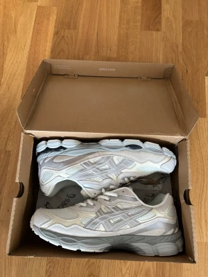 Vita Asics sneakers med mesh och skinn - Snygga vita sneakers från Asics med detaljer i mesh och skinn. Skorna har en chunky sula och klassisk Asics-logga på sidan. Färgen är en mix av vitt och ljusgrått, och de har Ortholite-innersula för extra komfort. Perfekta för en sportig och trendig look.