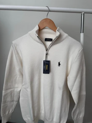 Vit Polo Ralph Lauren - Vit stickad tröja med halvzip från Polo Ralph Lauren. Perfekt för en clean och stilren look.