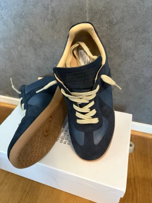 Maison margiela st 42 - Ett par mörkblåa maison margiela i storlek 42, de är i ganska bra skick (8/10), lite slitna vid tungan& insidan, har tagit väldigt bra hand om de annars. Det som medföljer är Lådan, kvitto (ÄKTHETSBEVIS) syns i bilden. Skriv om du har någon fundering🙌