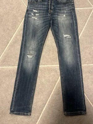 Slim fit jeans från Jack & Jones - Mörkblå slim fit jeans från Jack & Jones, modell Glenn. Jeansen har slitna detaljer och hål på benen för en trendig look. Klassisk femficksmodell med dragkedja och knapp. Perfekta för dig som gillar en smal passform och streetstil. En liten defekt vid gylfen därför ja säljer så lågt annars ny pris 799!