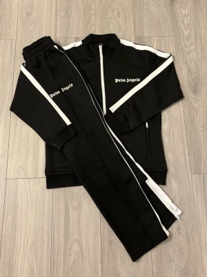 Palm Angels svart tracksuit set - Snyggt svart tracksuit set från Palm Angels med vita ränder längs ärmar och ben. Perfekt för sommaren. Fungerar i spontana men även fina sammanhang. Fraktas direkt vid köp! Fråga gärna om din storlek osv. Jag jobbar själv med kläder så jag kan storlekar bra. Finns i flertal färger då jag vunnit på auktion. Vid flera köp får du ett bra paketpris. 